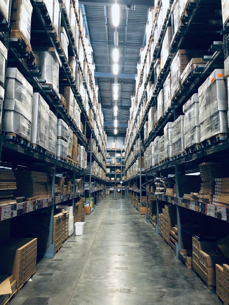 Narrow aisle between tall racks stacked with shrink-wrapped pallets