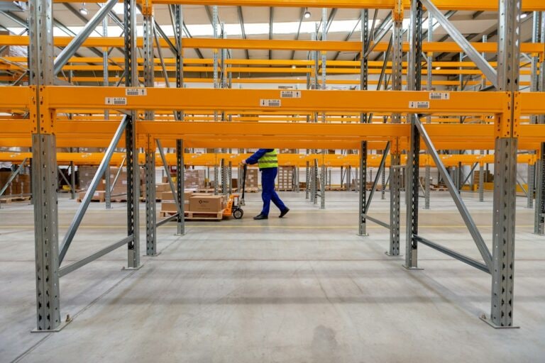 Worker moving a pallet with a hand truck past racking labelled A-187 to A-191
